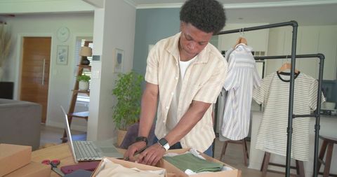 African american man packing apparel for online boutique in open-plan home workspace