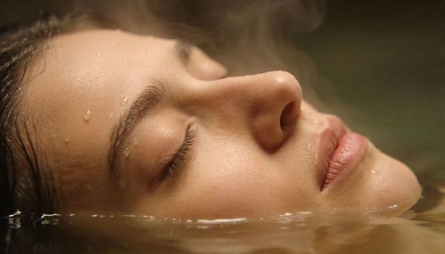Closeup floating female face in steaming water, serene wet skin portrait for wellness