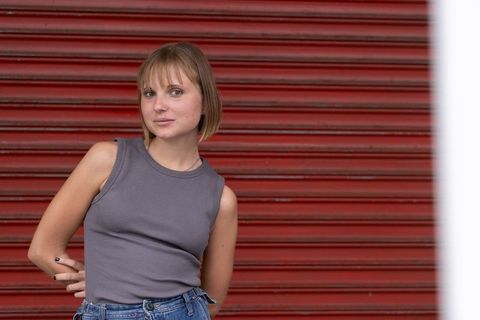 Young woman leaning on red shutter wearing tank top and hoop nose ring urban portrait
