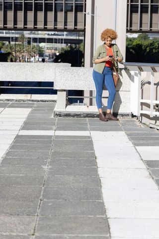 African american woman leaning on urban terrace checking smartphone in casual streetstyle