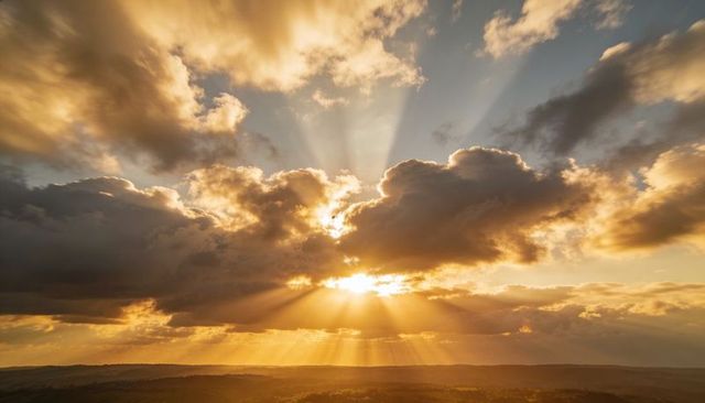Golden sunbeams streaming through layered clouds over rolling hills at golden hour