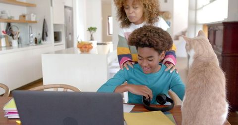 Mother and Son Bonding with Pet Cat in Kitchen Utilizing Laptop
