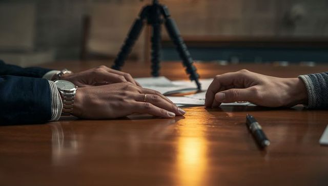 Business hands resting on documents during contract negotiation on wood conference table