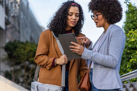 Two professional women collaborating outdoors using tablet on urban walkway