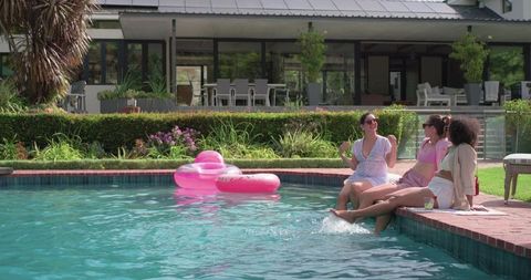 Friends laughing and dipping feet in backyard pool on sunny summer afternoon