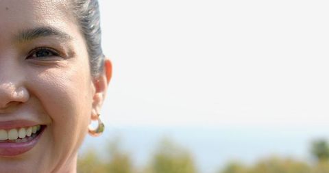 Smiling mid-adult woman wearing gold hoop earring near coastal horizon with copy space