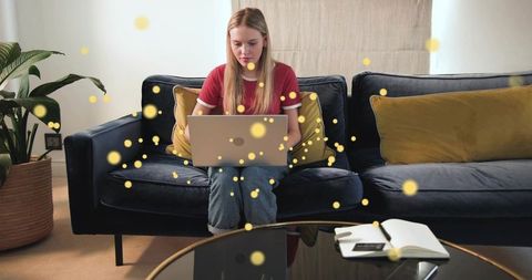 Young woman typing on laptop while sitting on navy sofa with cozy living room workspace