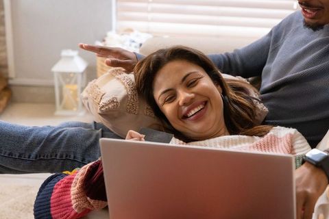Couple relaxing on couch while woman holding credit card using laptop for online shopping