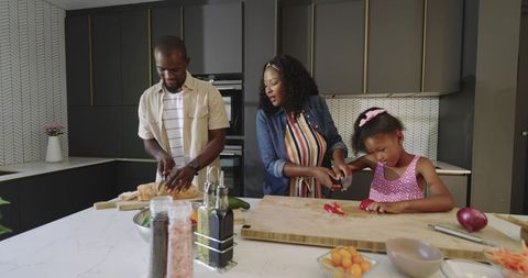 African American family cooking in modern kitchen chopping vegetables and slicing bread