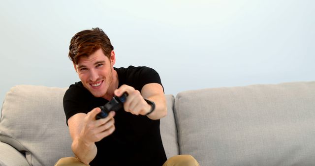 Young man in black shirt intensely playing video game on couch concentrating on challenge. Useful for promoting gaming consoles, indoor activities, and relaxation products.