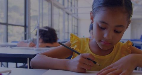 Elementary student concentrating while writing at sunny classroom desk with pencil