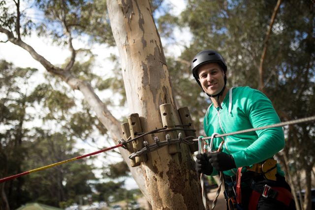 Smiling man attaching carabiner to rope in  adventure park