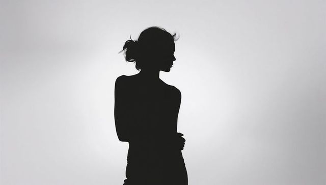 Minimal backlit female silhouette standing in studio with loose bun and fitted top