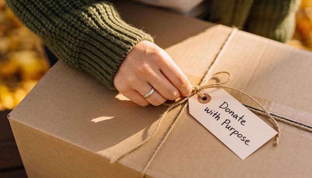Volunteer Tying Twine on Donation Box with 'Donate with Purpose' Tag in Autumn Light