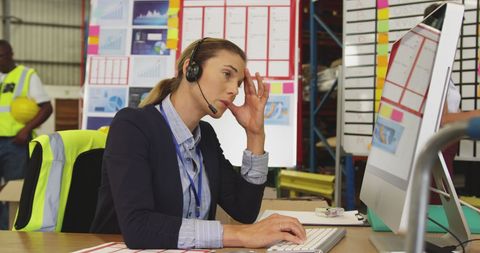 Female Warehouse Manager Multitasking with Computer and Headset