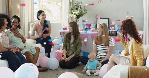Friends celebrating baby shower in living room with pastel balloons, gifts and cupcakes