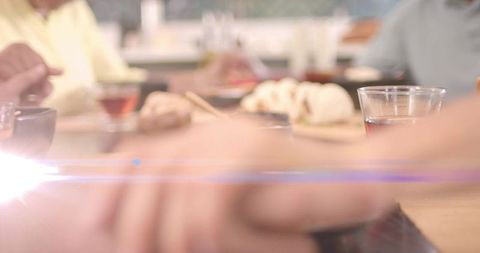 Friends reaching hands across wooden table during casual dumpling meal with warm lens flare