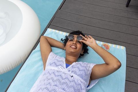 Indian woman relaxing on poolside towel wearing lace cover-up and sunglasses summer lifestyle