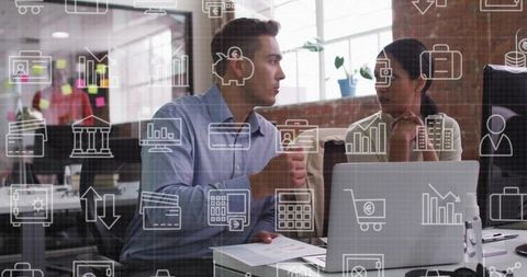 Colleagues discussing strategy with laptop and finance icons overlay in modern workspace