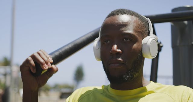 Focused man wearing headphones while exercising outdoors at a park. He is using fitness equipment and appears concentrated, suggesting a dedication to physical fitness. Suitable for topics on fitness, health, outdoor activities, concentration during workouts, and lifestyle inspiration.