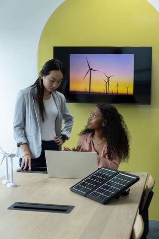 Asian and Black Female Engineers Collaborating on Solar and Wind Energy Project Meeting
