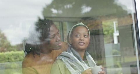 African American Couple Sharing Cozy Morning Moment by Window Holding Mug and Embracing