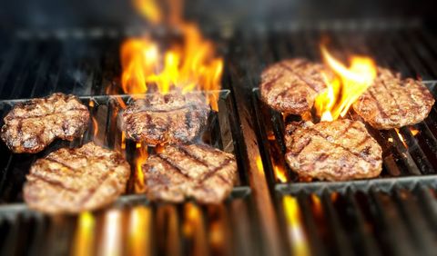 Grilling juicy beef burger patties over flame with charred grill marks and sizzling heat