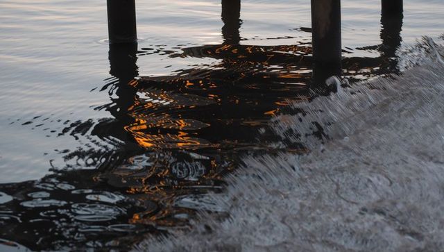 Pier pilings casting amber reflections on rippling surf at sunrise with foamy shoreline