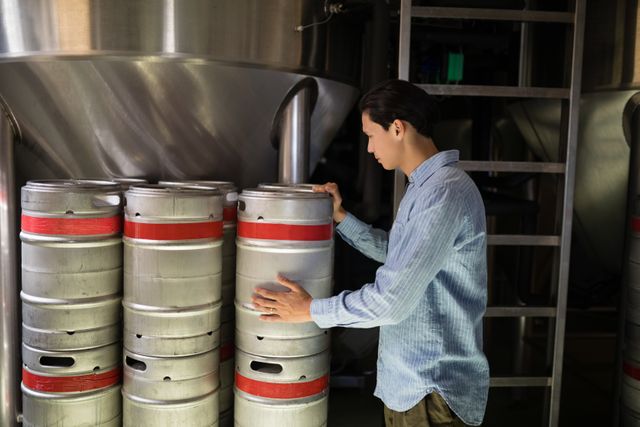 Manager inspecting beer kegs in brewery warehouse, ensuring quality control and inventory management. Useful for illustrating industrial processes, beverage industry operations, and logistics management in a brewery or restaurant setting.
