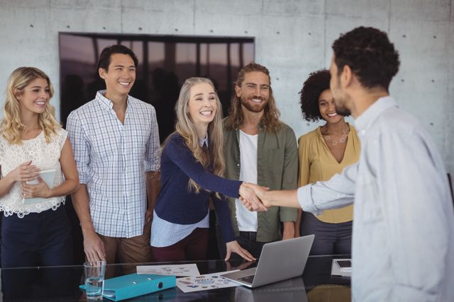 Smiling young business people shaking hands at desk in creative office