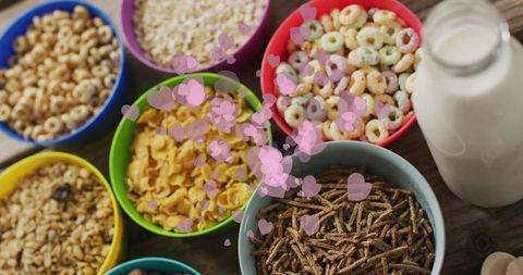 Colorful breakfast cereal bowls sitting on wooden table with milk jar and pink heart bokeh