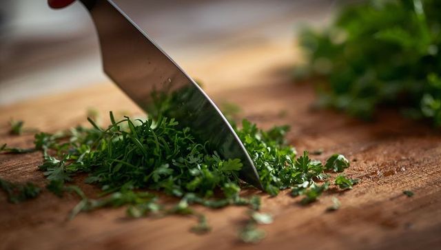 Close-up of Chef Knife Chopping Fresh Parsley on Wooden Board