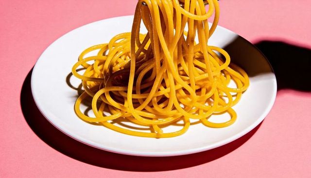 Vibrant golden spaghetti twirl on white plate over pink background minimalist food art