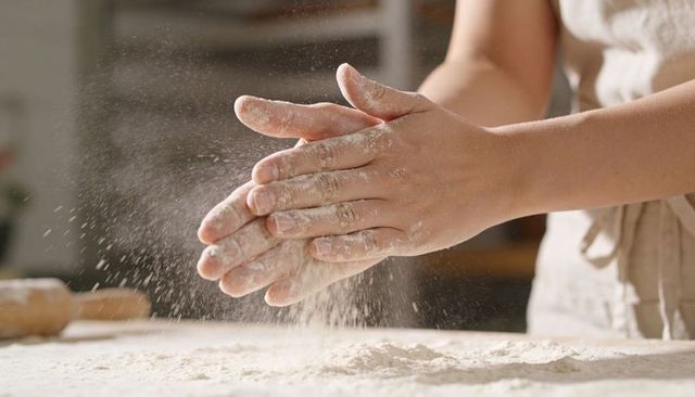 Clapping flour-dusted hands sending flour cloud over kitchen counter