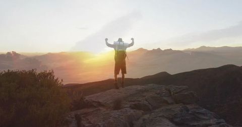 Depicts a hiker celebrating victory at the summit of a rocky mountain during a stunning sunset. It signifies exploration and conquering challenges with determination, making it perfect for content relating to adventure, travel dreams, or personal growth. Can be used for motivational purposes or in advertisements encouraging outdoor pursuits.