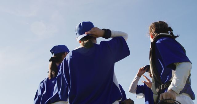 Captures youth baseball team gathering on field in blue uniforms under clear sky. Perfect for themes involving youth sports, teamwork, outdoor activities, and team games. Could be used in sports equipment advertising, children sports campaigns, or community sports programs promotions.