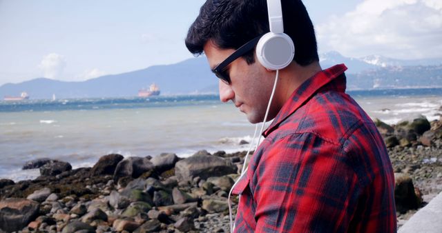 Man Wearing Headphones Listening to Music by Seaside Rocky Shoreline - Download Free Stock Images Pikwizard.com