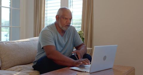 Senior African American Man Engaging with Laptop and Smartphone at Home