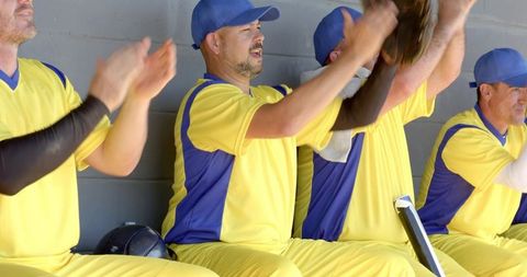 Baseball teammates cheering and clapping in dugout wearing yellow blue uniforms
