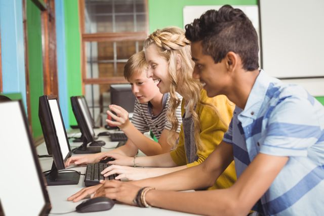 Three smiling students sit at a row of computers in a brightly colored classroom, engaging in learning activities. Ideal for illustrating educational concepts, technology in the classroom, teamwork, and joyful learning environments.