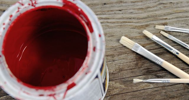 Open red paint can with paintbrushes on rustic wooden surface. Ideal for use in DIY project tutorials, art and crafts blogs, or promotional materials for art supplies. Can also be used in themes related to creativity and home improvement.