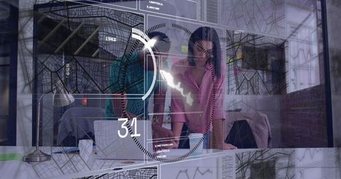 Colleagues leaning over laptop collaborating with HUD analytics on glass partition desk