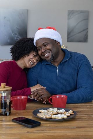 African american couple sharing cozy christmas moment with santa hat, coffee and cookies