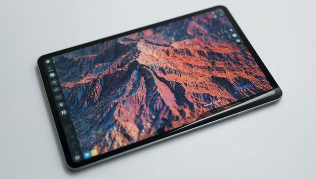 Slim metal tablet displaying mountain wallpaper with left app dock and ultrathin bezel