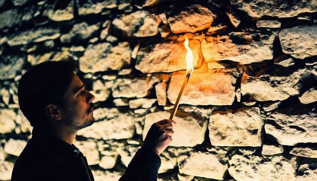 Man holding burning torch inspecting stone tunnel wall by firelight in underground cellar