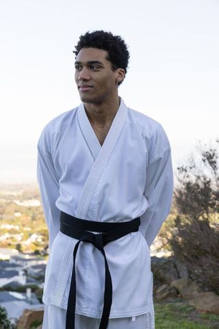 Man wearing karate gi and black belt on quiet hilltop