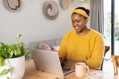 African american woman working from home on laptop in cozy sunlit workspace with plants