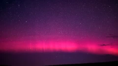 Magenta aurora band streaming vertical rays across starry night sky timelapse