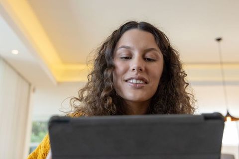 Young woman looking at tablet holding case wearing mustard-yellow sweater in modern home