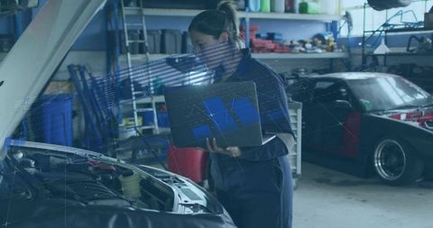 Female mechanic inspecting engine holding laptop running digital diagnostics in workshop